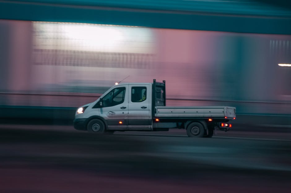 A professional removals team member from manandvanfulham.co.uk is inside a bright, spacious room with large arched windows allowing natural light, preparing for a home relocation. The worker, dressed 