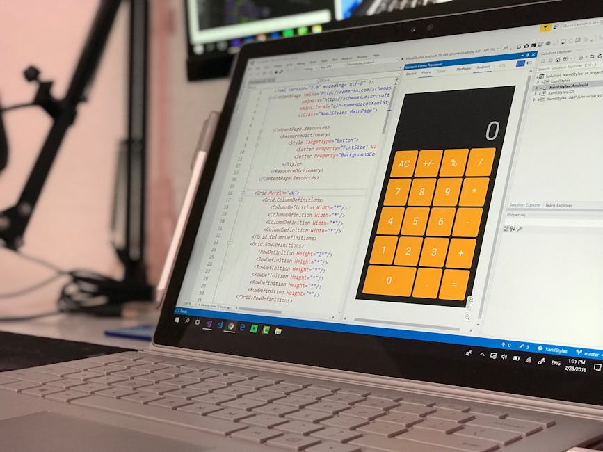 A close-up of a laptop computer on a desk displaying a software development environment with HTML and CSS code on the left side of the screen, and a digital calculator interface with orange buttons an